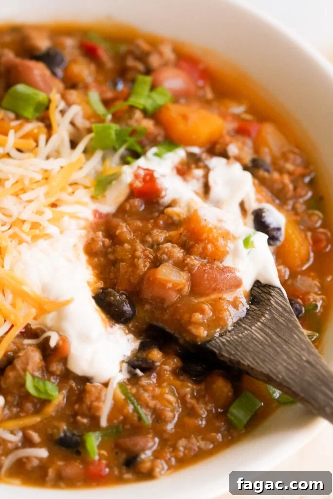 Hearty Butternut Squash and Turkey Chili Recipe 2 butternut squash turkey chili in a bowl with sour cream and cheddar cheese, spoon taking a spoonful