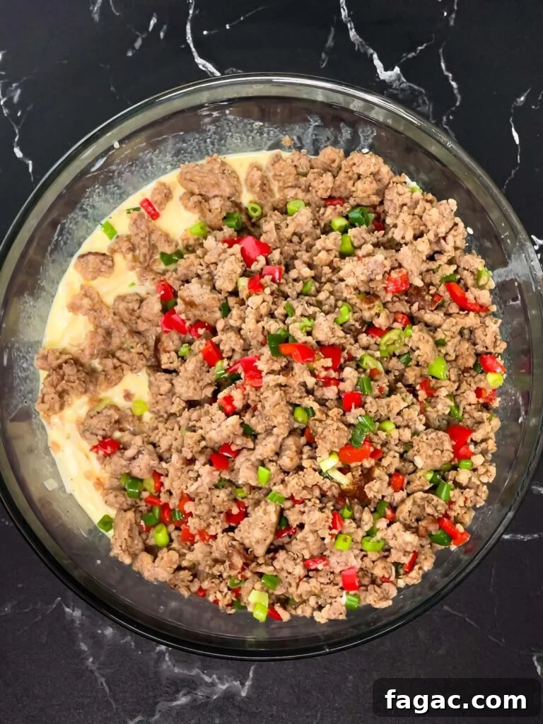 Sausage and Hashbrown Breakfast Casserole for 12 Guests 12 Cooked sausage mixture added on top of egg and hash brown mixture in a bowl.