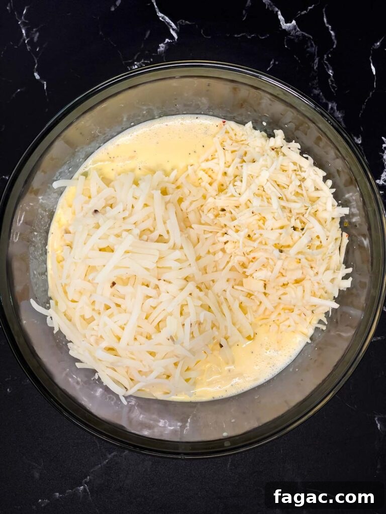 Sausage and Hashbrown Breakfast Casserole for 12 Guests 10 Whisked egg mixture with shredded hash browns and cheese added on top in a mixing bowl.