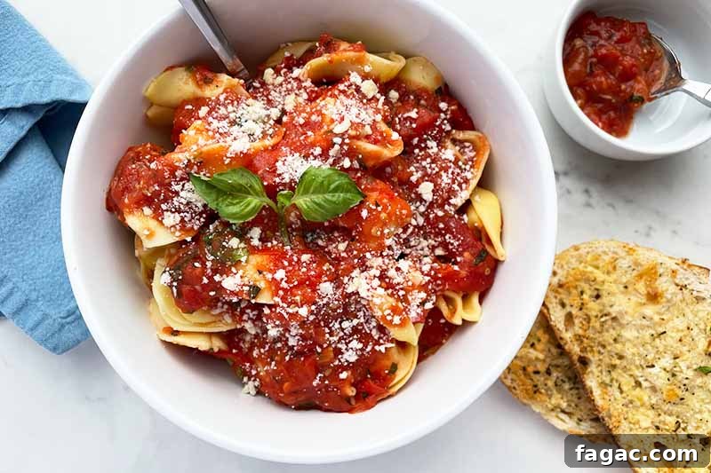 Oven-Roasted Tomato Sauce Recipe for Rich Homemade Flavor 11 Horizontal image of a white bowl with pasta and marinara next to garlic bread and a blue napkin.