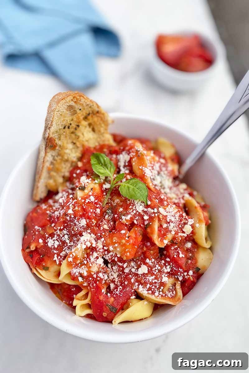 Oven-Roasted Tomato Sauce Recipe for Rich Homemade Flavor 5 Vertical image of a white bowl with pasta and a red sauce with garlic bread next to a blue napkin.