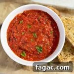 Horizontal image of a white bowl with a red sauce next to slices of garlic bread on a parchment paper lined baking sheet.