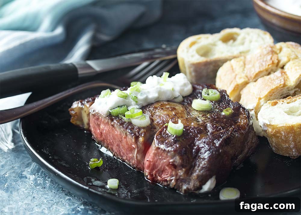 Cut open medium rare ribeye on a plate with horseradish sauce and bread.