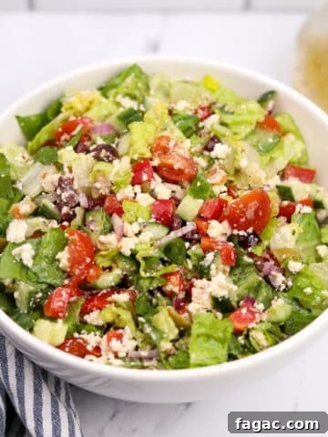 A white bowl filled with a leafy salad and Greek-inspired vegetables.