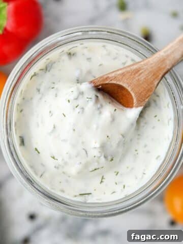 Scooping ranch dressing from a glass jar with a wooden spoon.