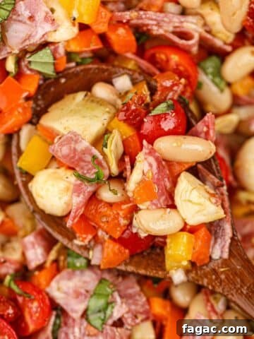 A wooden spoon scooping a portion of bean salad with sun-dried tomatoes, mozzarella, and basil.