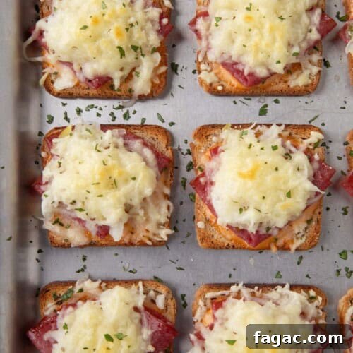 mini reuben sandwiches with a square of toasted rye bread topped with corned beef and melted swiss cheese on a sheet pan.