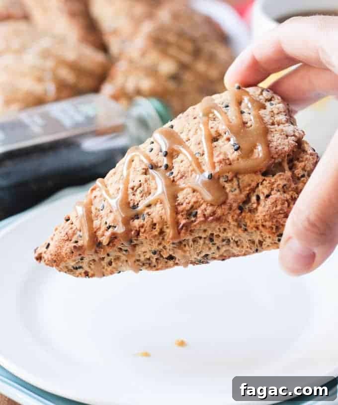 Banana Black Sesame Vegan Scones - easy dairy free scones with a surprisingly delightful flavor combo. Just sweet enough with no refined sugar. They have the perfect balance of sweet and nutty. You've gotta try these amazing scones - breakfast, brunch, tea time, even dessert! Hand holding an eggless scone drizzled with Maple Tahini Glaze.