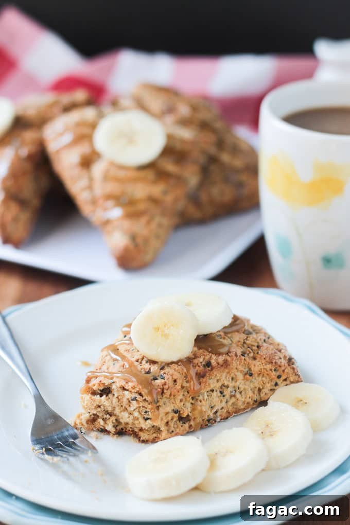 Banana Black Sesame Vegan Scones - easy dairy free scones with a surprisingly delightful flavor combo. Just sweet enough with no refined sugar. They have the perfect balance of sweet and nutty. You've gotta try these amazing scones - breakfast, brunch, tea time, even dessert! Bite taken out of a banana scone on a white plate topped with two slices of fresh banana.