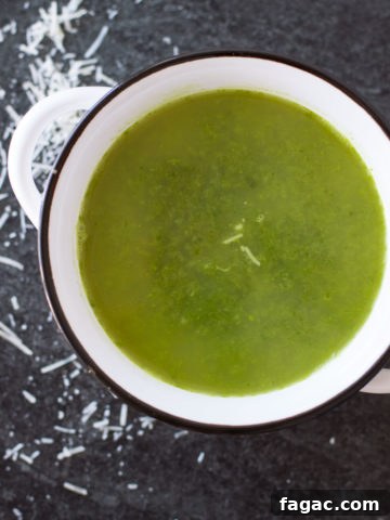 White bowl containing kale and leek soup, shredded Parmesan cheese on table.