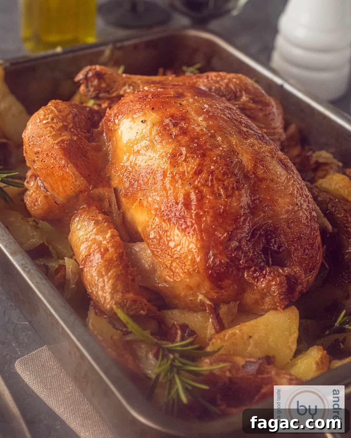 Crispy Roast Chicken with Herbed Potatoes Recipe 2 A height picture of a casserole filled with whole roast chicken, potatoes, rosemary, and bacon.