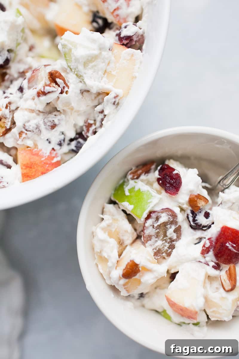 Festive Creamy Fruit Salad Recipe for Christmas Parties 2 White bowls with creamy whipped cream topped fruit salad with red and green apples, grapes, bananas, cranberries and pecans.