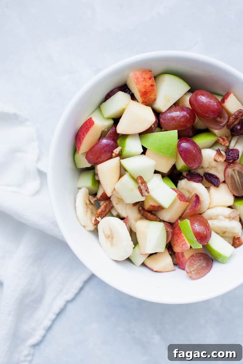 Festive Creamy Fruit Salad Recipe for Christmas Parties 5 White bowl with red and green apples, pecans, grapes, bananas, and cranberries.