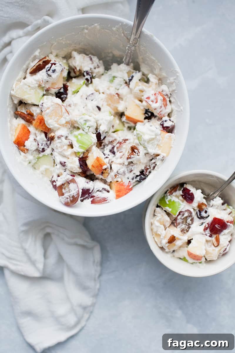 Festive Creamy Fruit Salad Recipe for Christmas Parties 6 White bowls with creamy whipped cream topped fruit salad with red and green apples, grapes, bananas, cranberries and pecans.