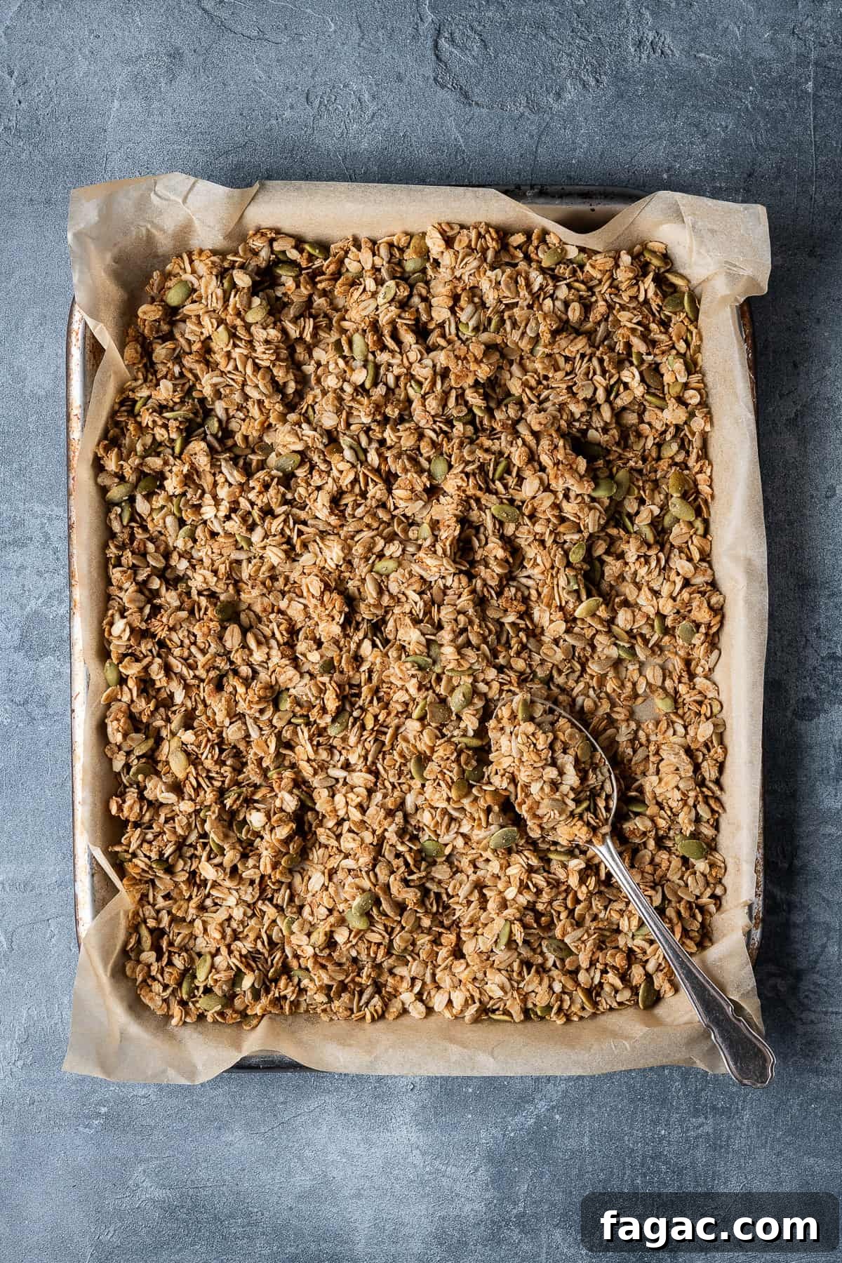 Baked vegan granola A baking parchment lined tray of granola on a grey background.