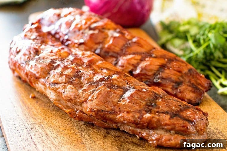 BBQ Pork Tenderloin Recipe: Juicy Grilled Pork Tenderloin Tips 3 Two bbq pork tenderloins laying on wood cutting board with purple onion and parlsey in background.