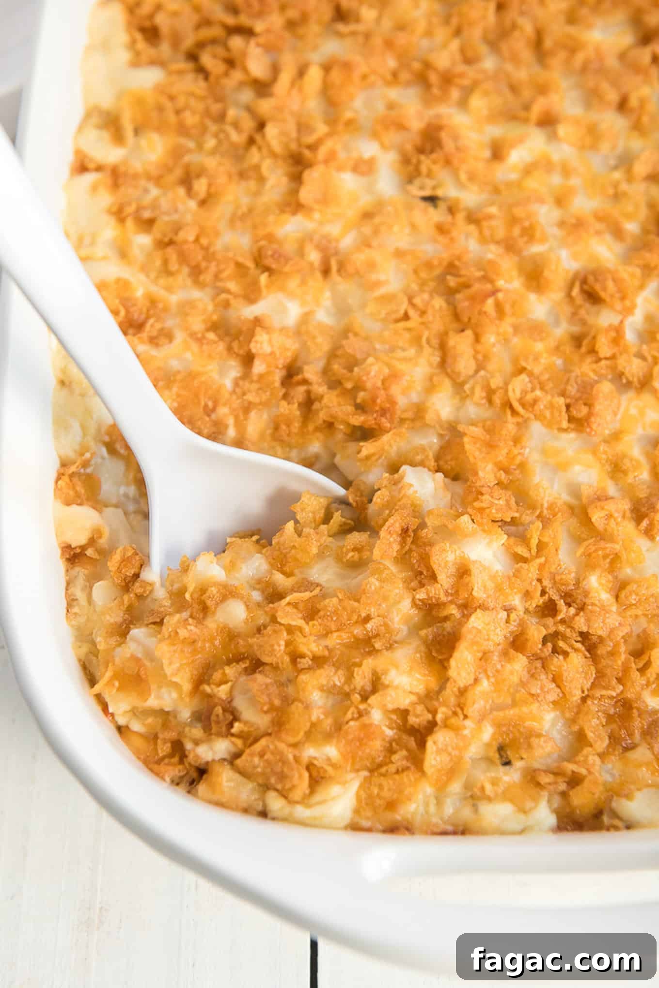 A spoon dipping into a dish of cheesy hash brown casserole.