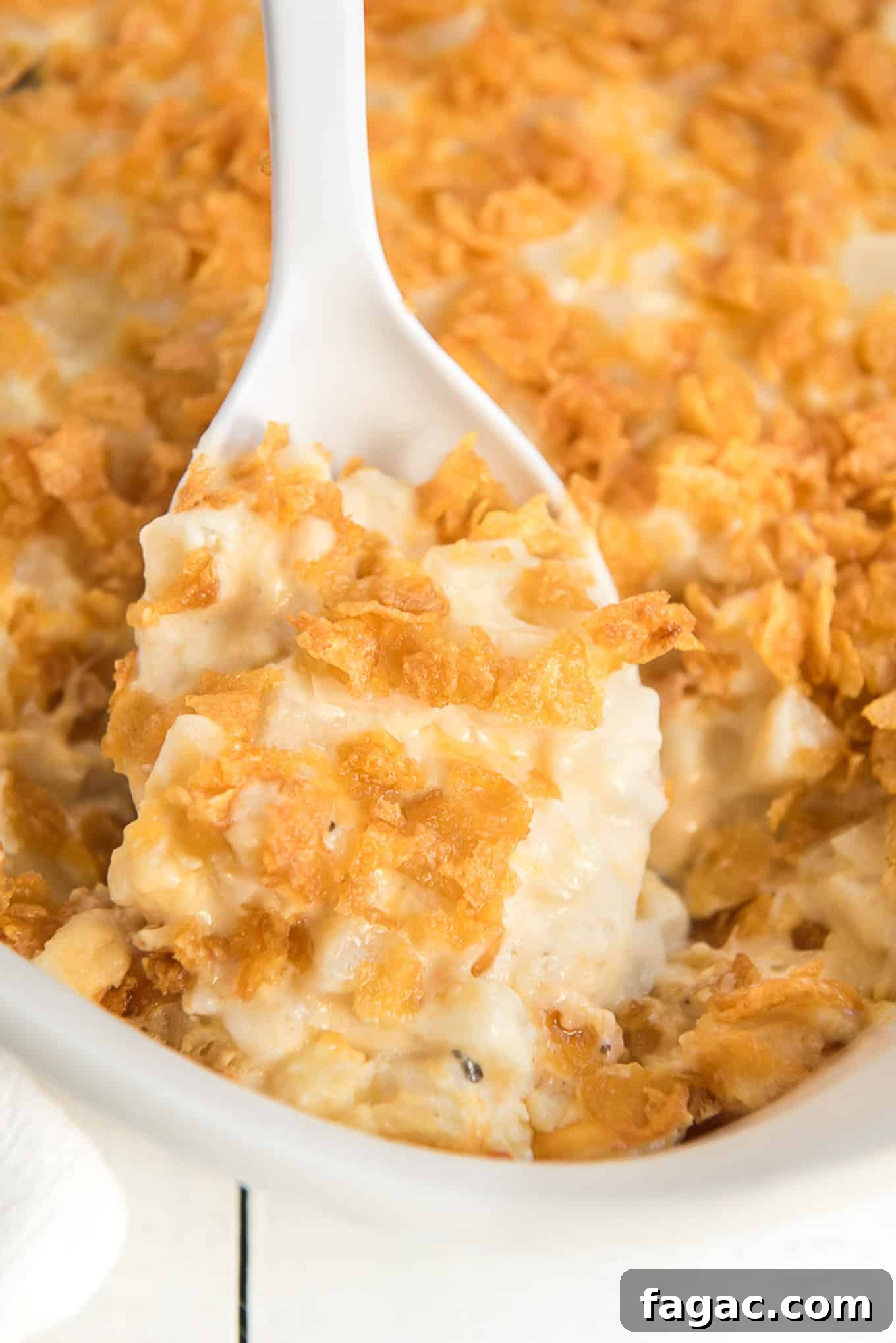 A spoon dipping into the casserole dish to pick up a serving of cheesy potatoes with corn flakes.