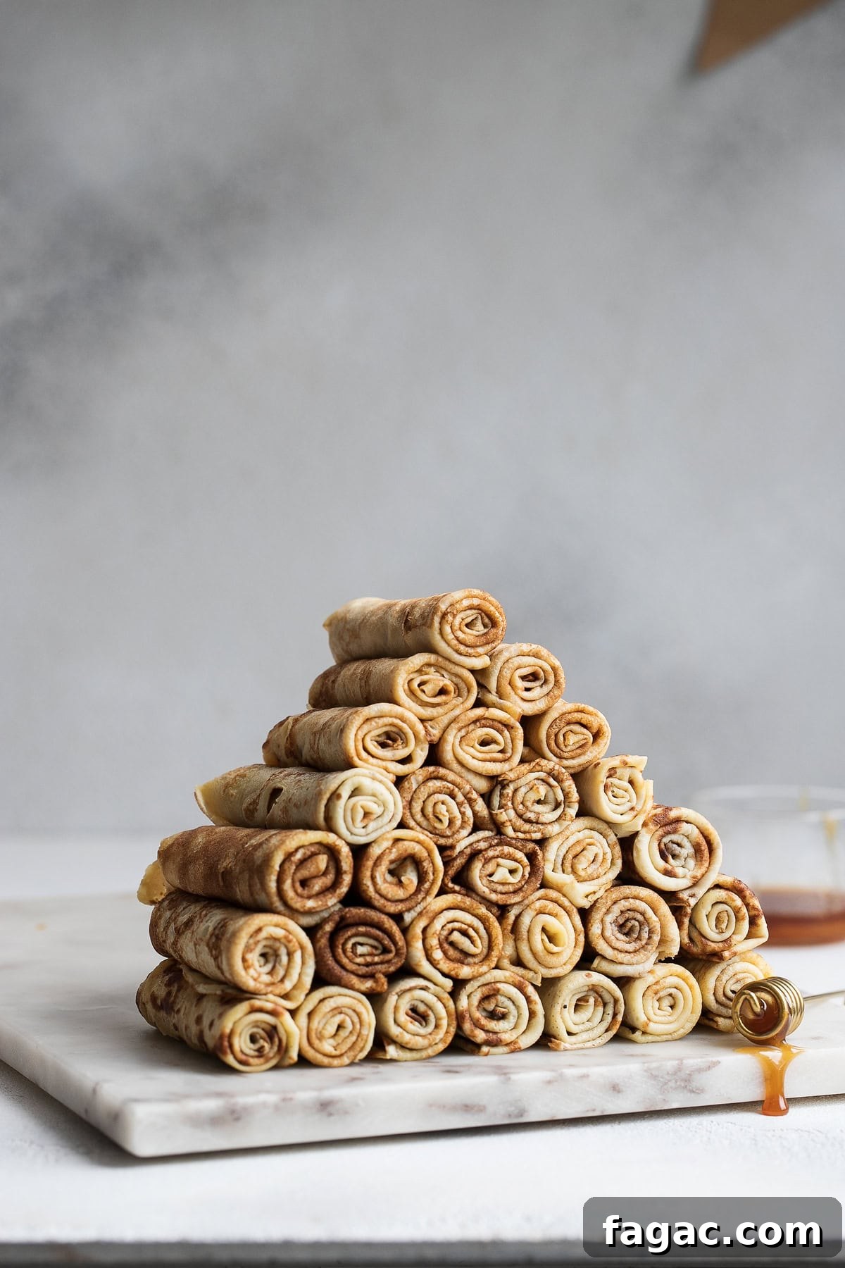 Rolled Polish crepes arranged in a pyramid on a marble board.