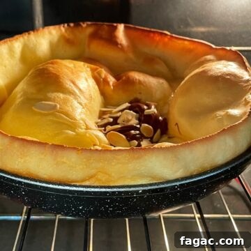 Puffed vanilla Dutch baby pancake topped with Nutella and flaked almonds in the oven.