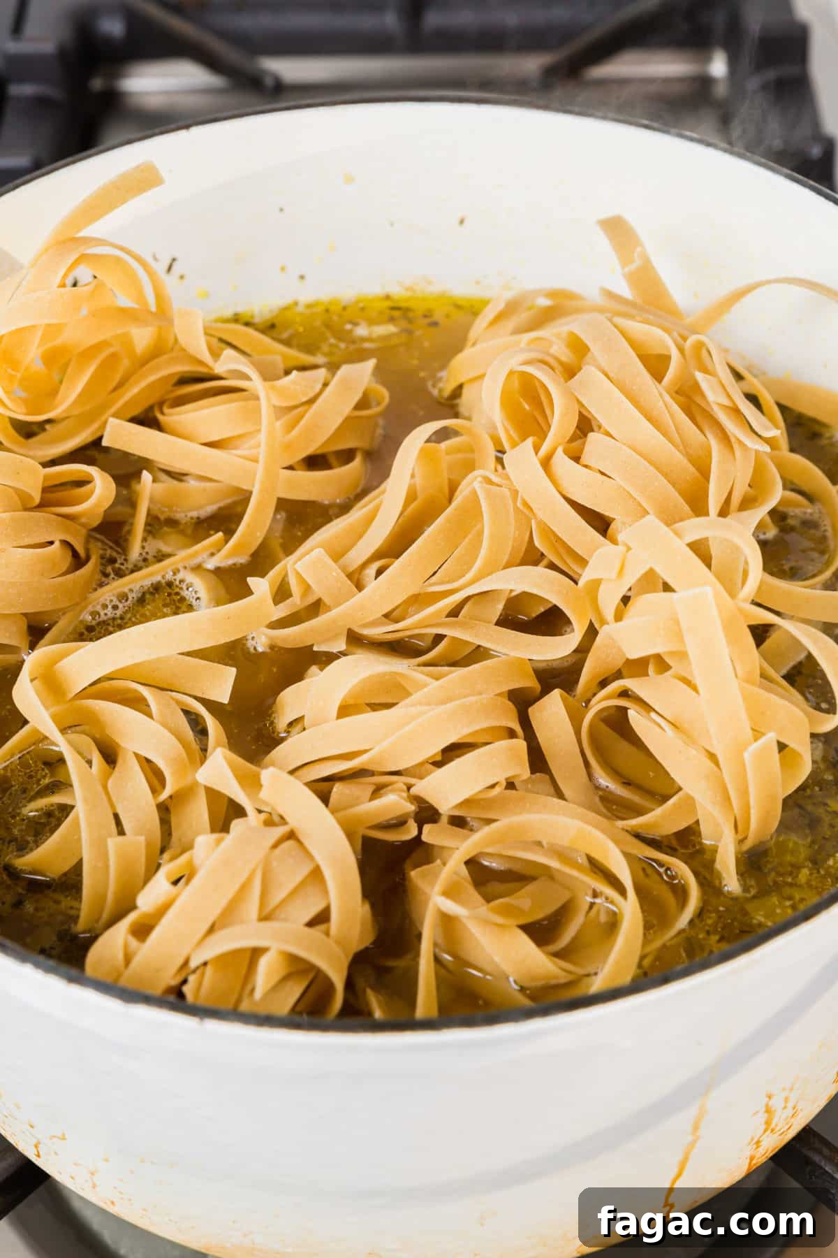 Comforting Gluten-Free Chicken Noodle Soup Recipe 11 A white dutch oven of gluten free egg noodles added to a pot of chicken noodle soup before the noodles have been cooked.