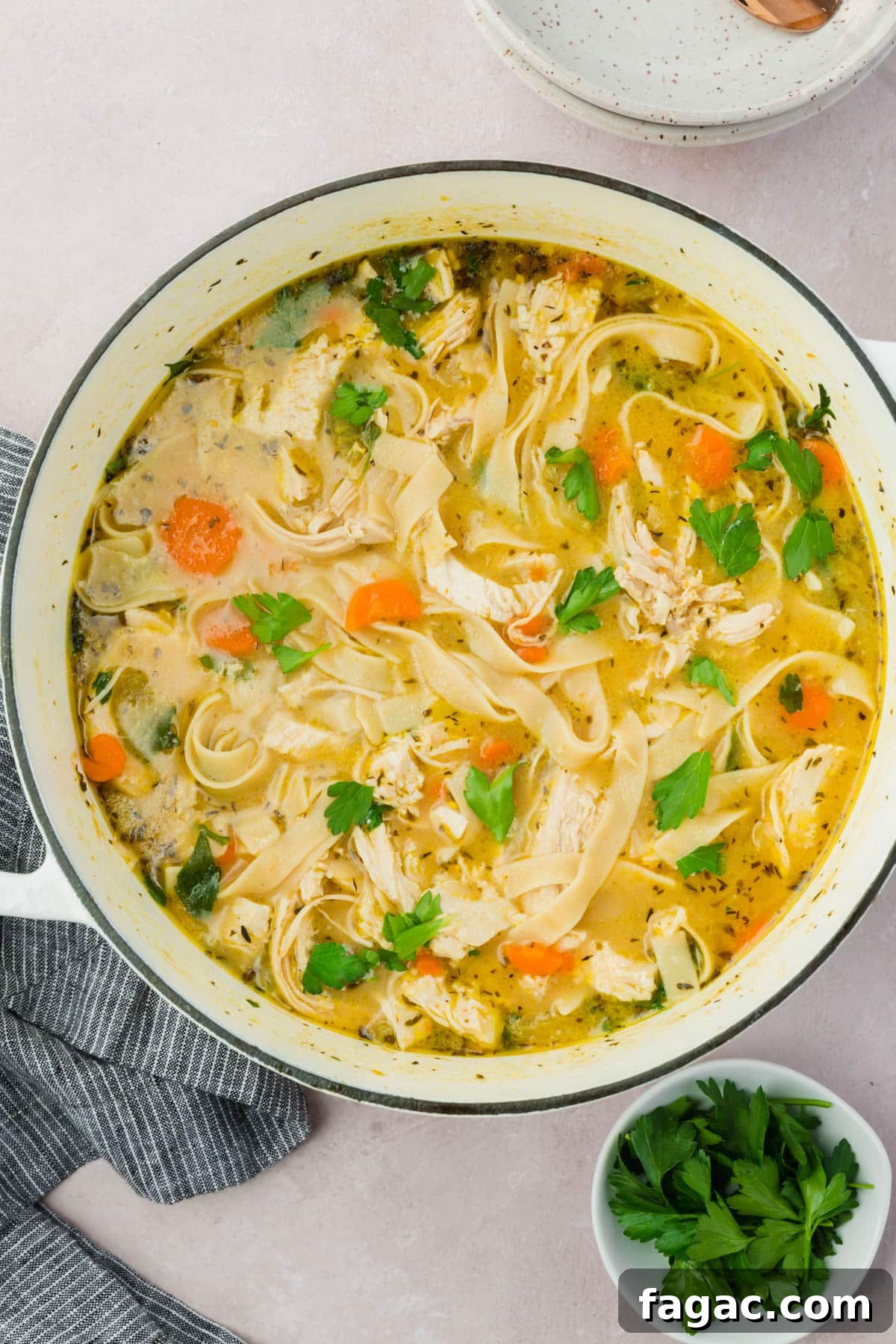 Comforting Gluten-Free Chicken Noodle Soup Recipe 13 A white dutch oven with gluten free chicken noodle soup topped with fresh chopped parsley.