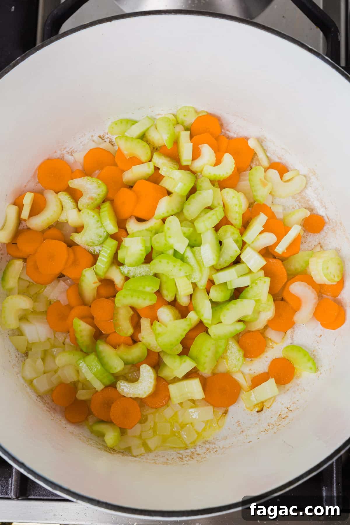 Comforting Gluten-Free Chicken Noodle Soup Recipe 4 An overhead view of a white dutch oven with raw diced celery, carrots and onion in olive oil before cooking.