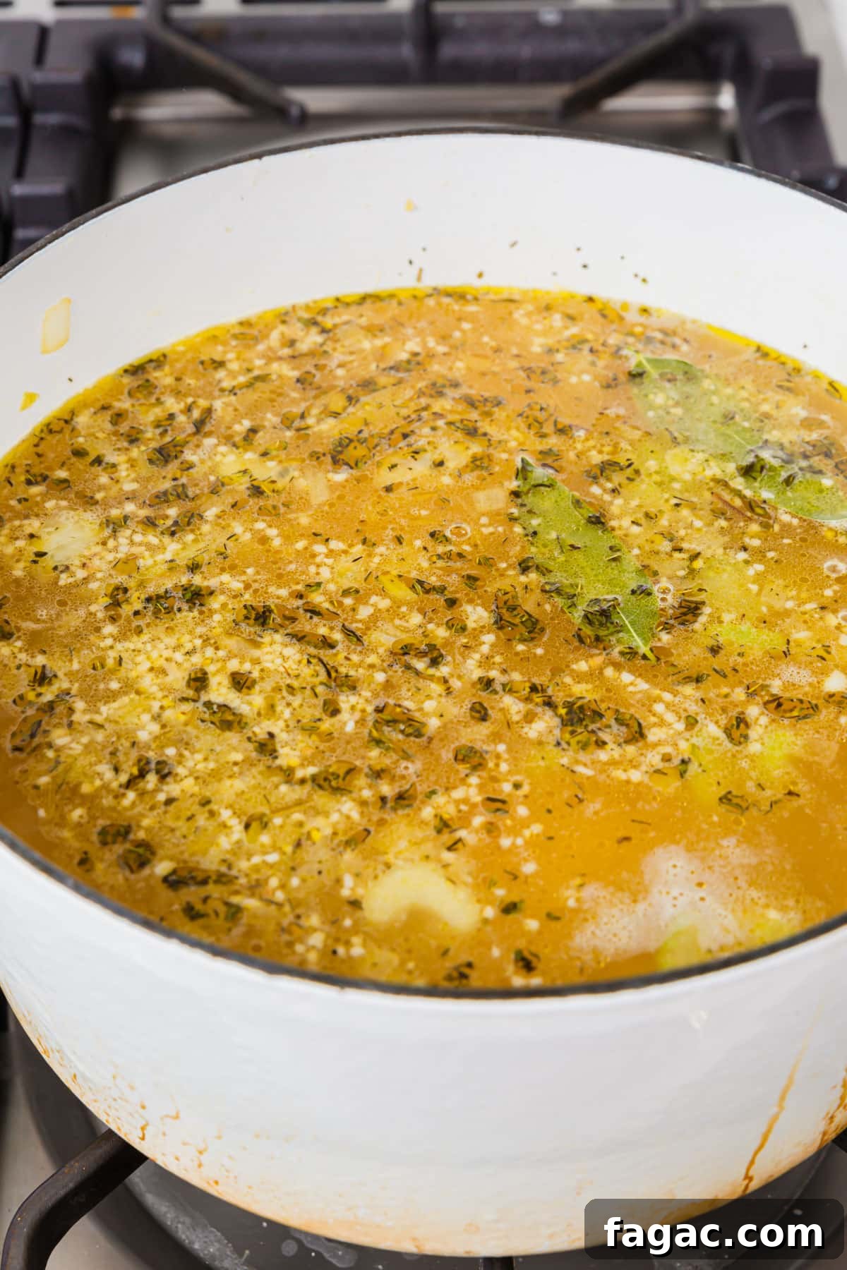 Comforting Gluten-Free Chicken Noodle Soup Recipe 9 A white dutch oven of chicken broth, spices, garlic, and bay leaves simmering on the stove top.