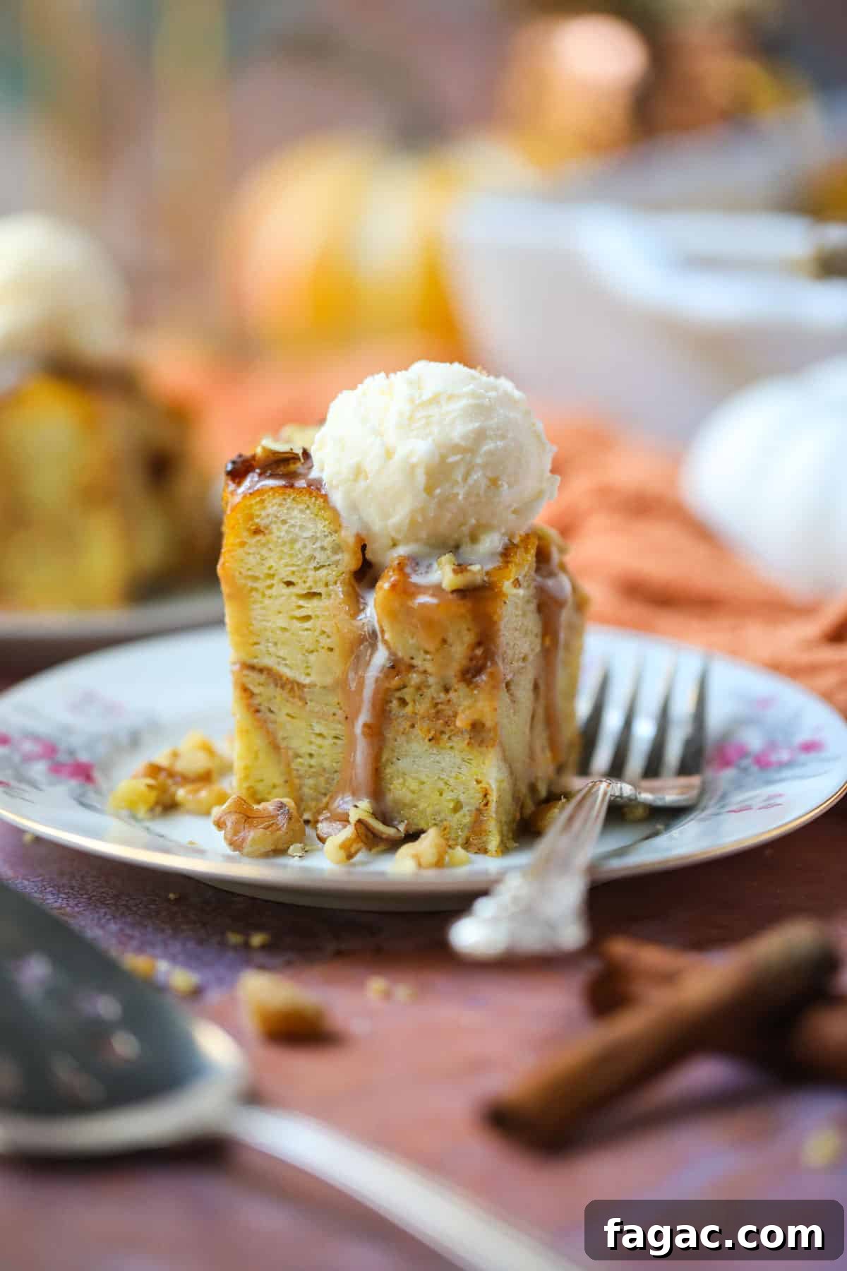 Salted Caramel Pumpkin Bread Pudding Recipe 2 A serving of pumpkin bread pudding with salted caramel sauce and vanilla ice cream on a white dessert plate with a silver fork.