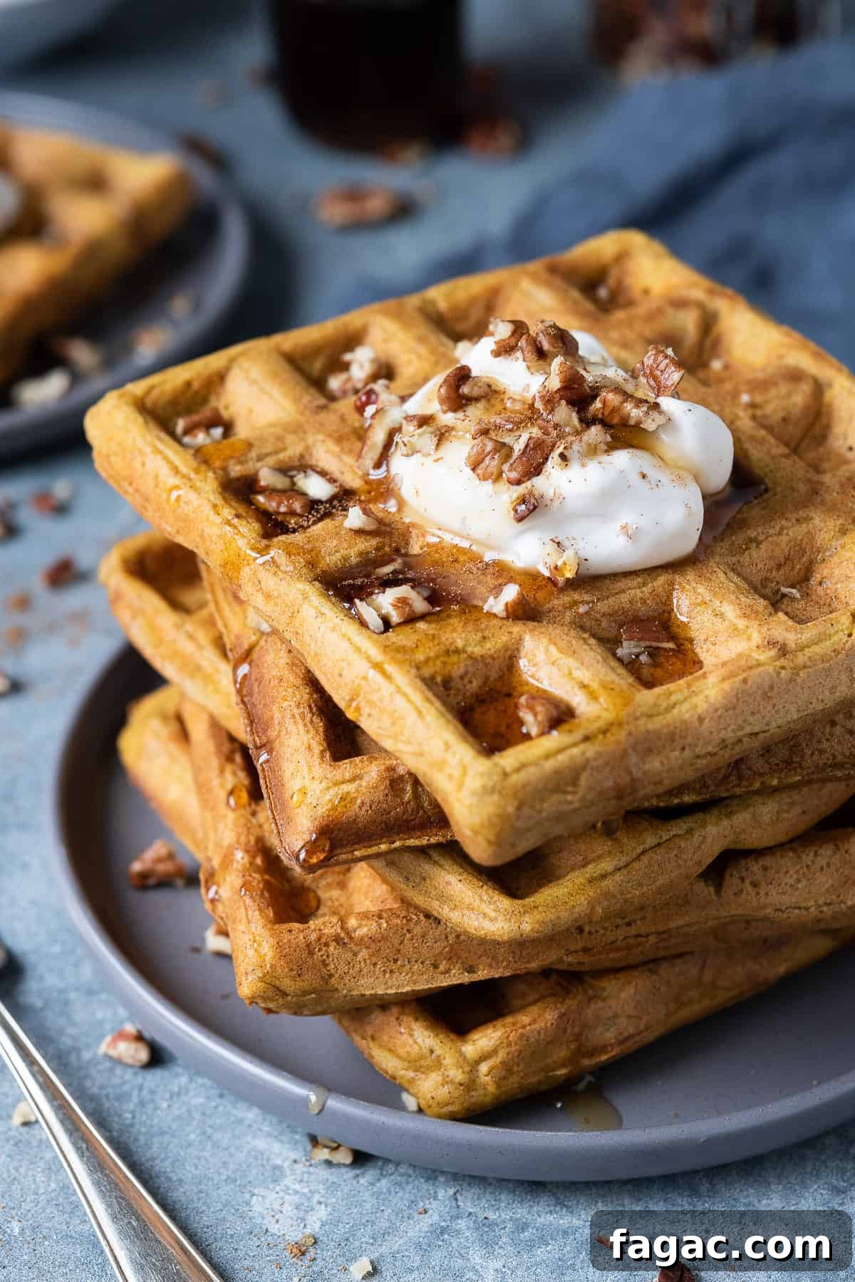 Vegan pumpkin waffles - these super fluffy vegan waffles are crispy on the outside and light and soft on the inside, you would never be able to tell that they are eggless and dairy-free! They are lightly spiced and flavoured with pumpkin, perfect for an autumnal breakfast or brunch! #veganbreakfast #veganbrunch #eggless #dairyfree A stack of vegan pumpkin waffles on a grey plate.