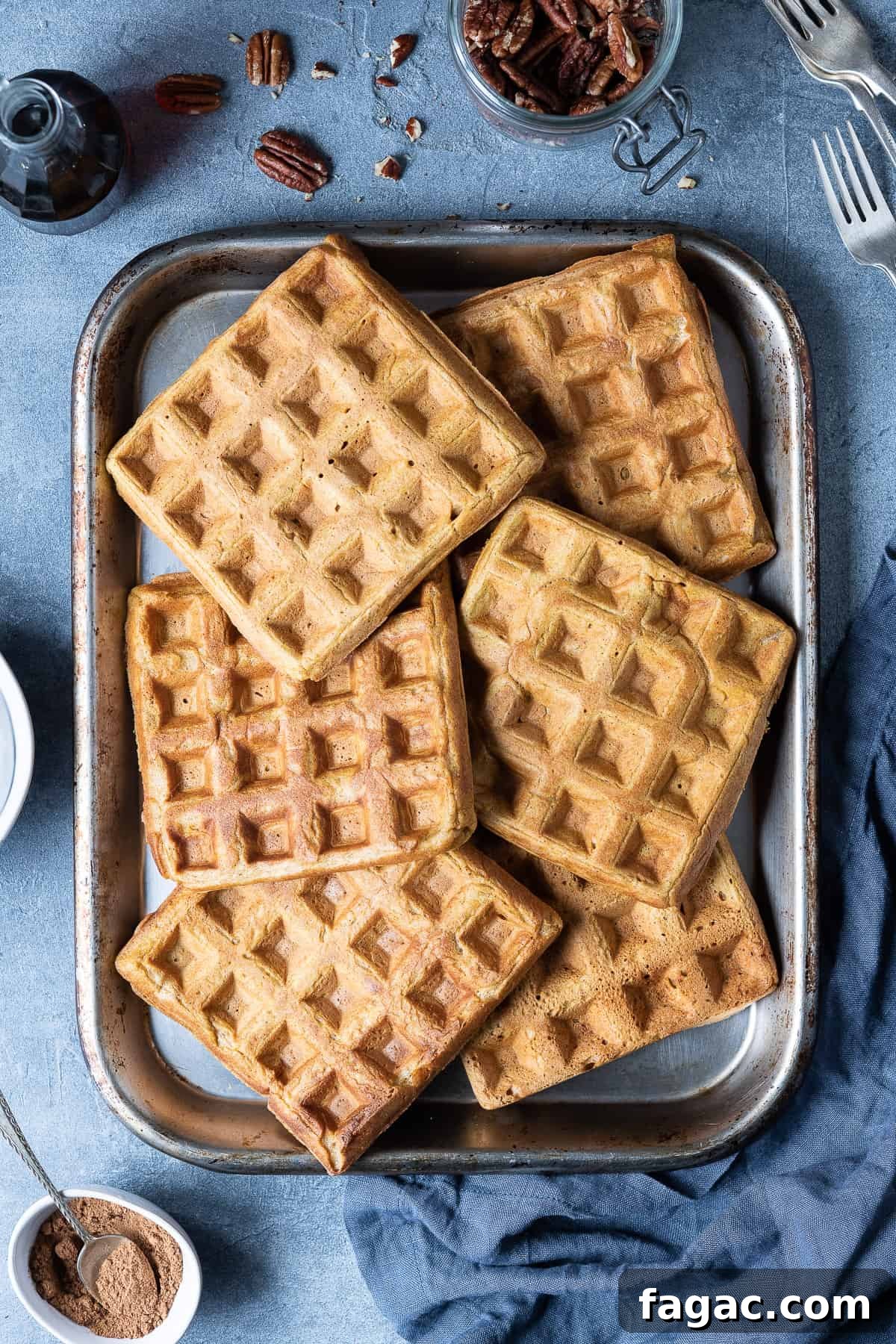 Vegan pumpkin waffles - these super fluffy vegan waffles are crispy on the outside and light and soft on the inside, you would never be able to tell that they are eggless and dairy-free! They are lightly spiced and flavoured with pumpkin, perfect for an autumnal breakfast or brunch! #veganbreakfast #veganbrunch #eggless #dairyfree Pumpkin waffles on a metal baking tray on a grey background.