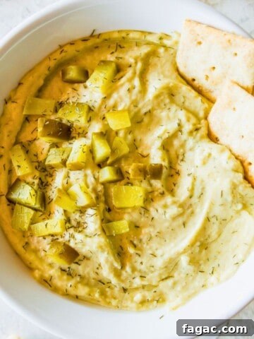 A bowl filled with a vegan dill pickle dip topped with chopped dill pickles and two crackers.