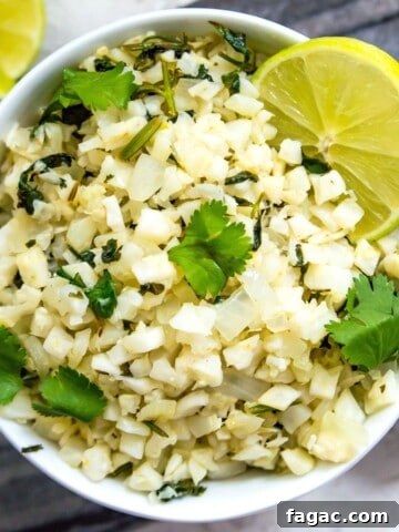 A bowl of cilantro lime cauliflower rice garnished with fresh cilantro and lime wedges.
