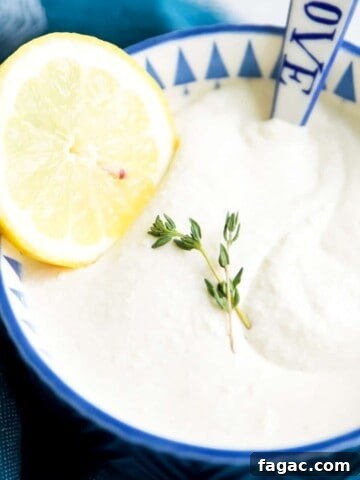 A bowl of dairy free sour cream with a spoon in it and a lemon slice on top.
