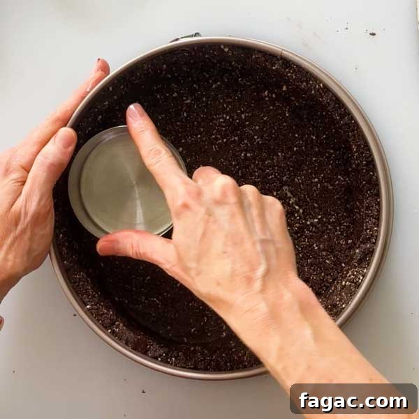 Pressing the crust into a springform pan using a measuring cup.