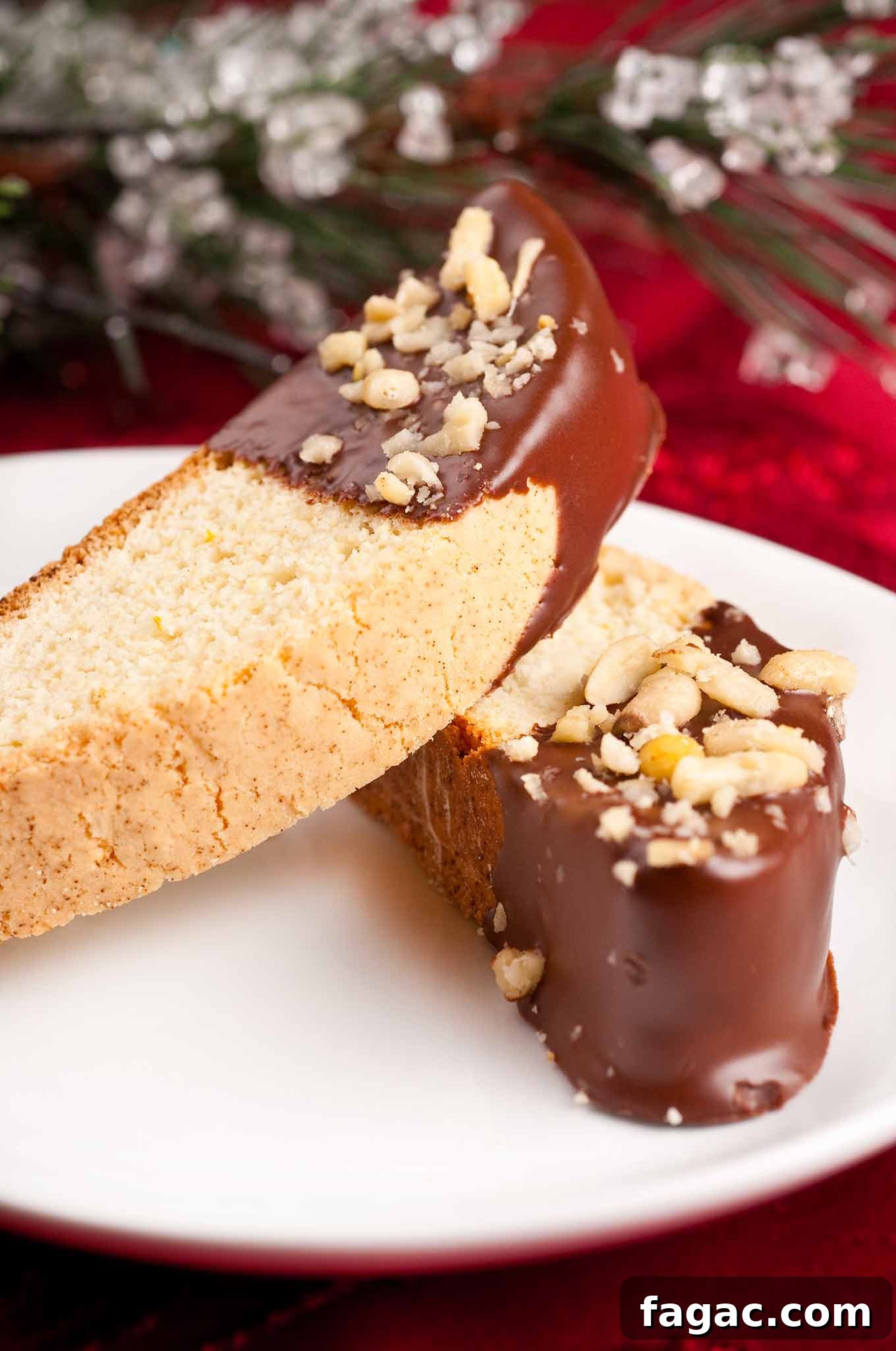 Buttery Orange Biscotti: Classic and Almond Variations 3 Two chocolate dipped orange biscotti on a white serving plate with Christmas table decor in the background.