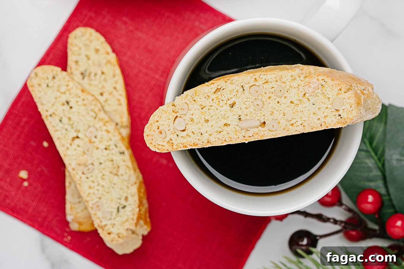 Buttery Orange Biscotti: Classic and Almond Variations 8 An overhead view of orange rosemary biscotti on top of a mug of coffee, a red napkin underneath, two more biscotti and a sprig of holly to the side.