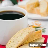 Buttery Orange Biscotti: Classic and Almond Variations 9 Buttery biscotti with orange, pine nuts, and rosemary on a red napkin next to a mug of coffee, more biscotti and Christmas table decor in the background.