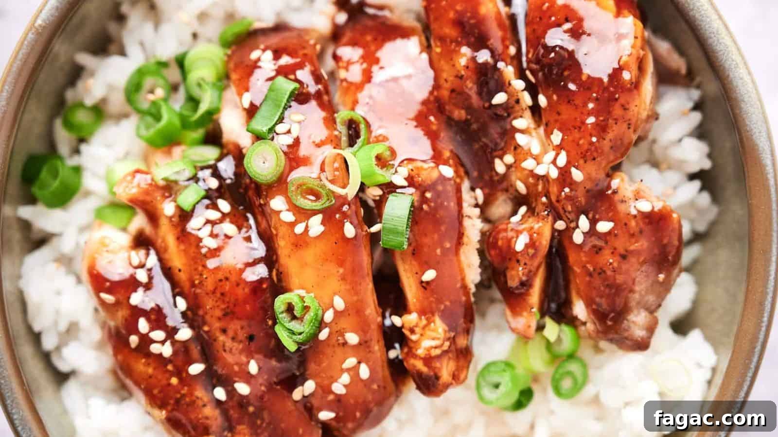 A bowl of white rice topped with glazed chicken and garnished with green onions and sesame seeds.