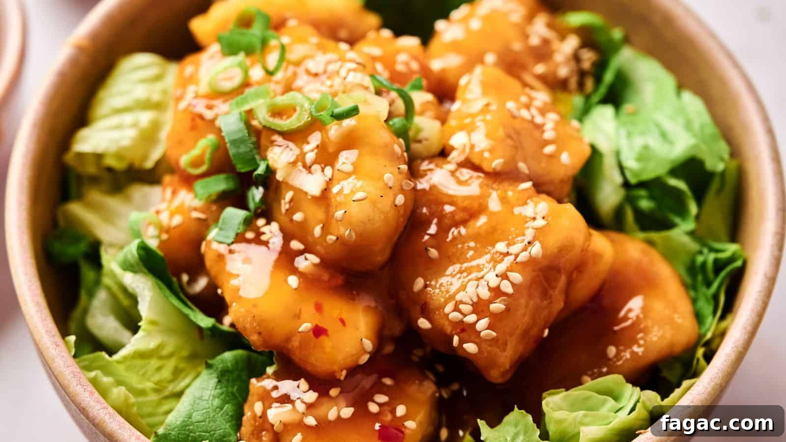 A bowl of crispy tofu coated in sesame sauce, garnished with green onions and sesame seeds, served on a bed of lettuce.