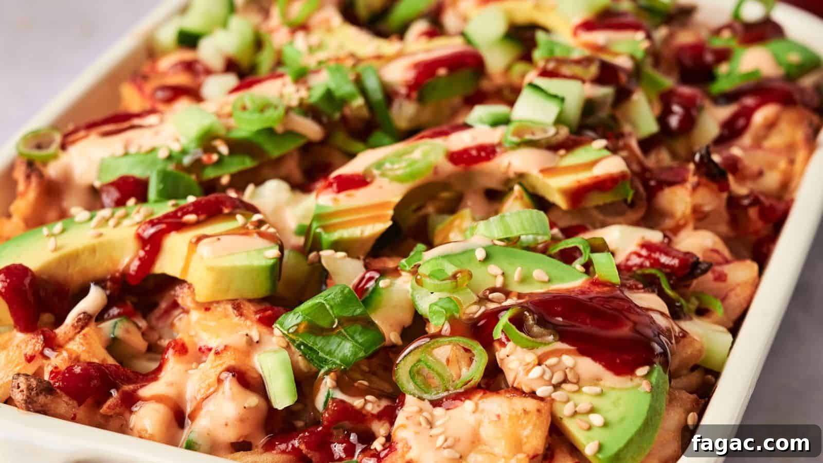 A dish of loaded fries inspired by sushi bake, topped with avocado slices, diced cucumbers, green onions, sesame seeds, and drizzled with sauce.