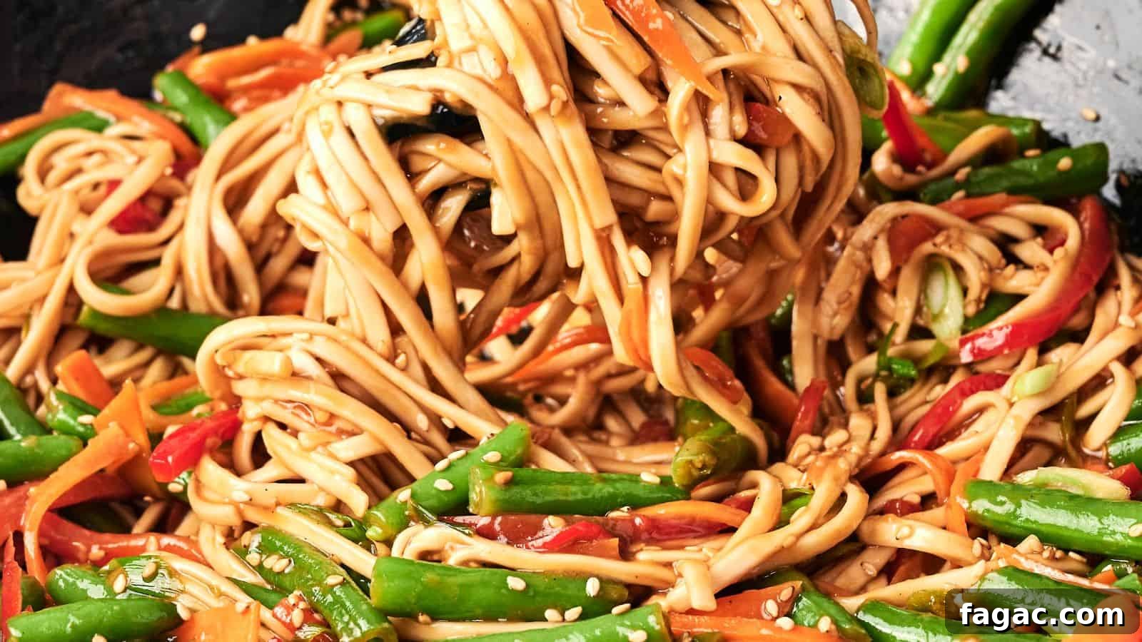 A close-up of stir-fried noodles with green beans, red bell peppers, and carrots, garnished with sesame seeds.