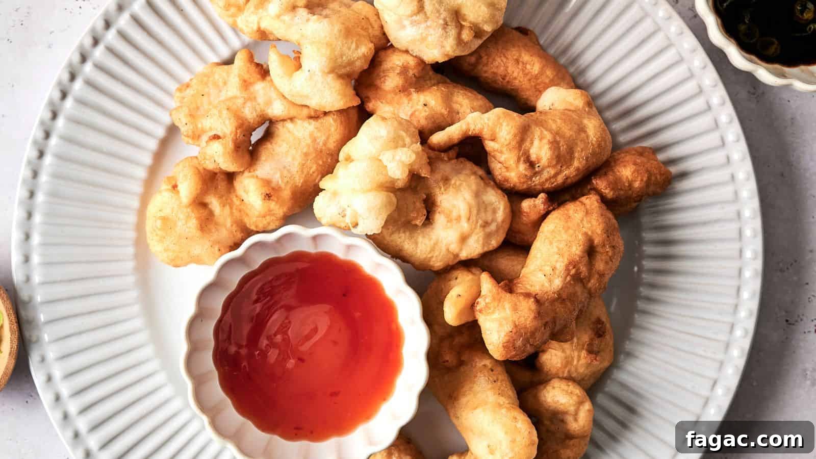 Plate of batter-fried fritters with a bowl of red dipping sauce on a white plate, viewed from above.