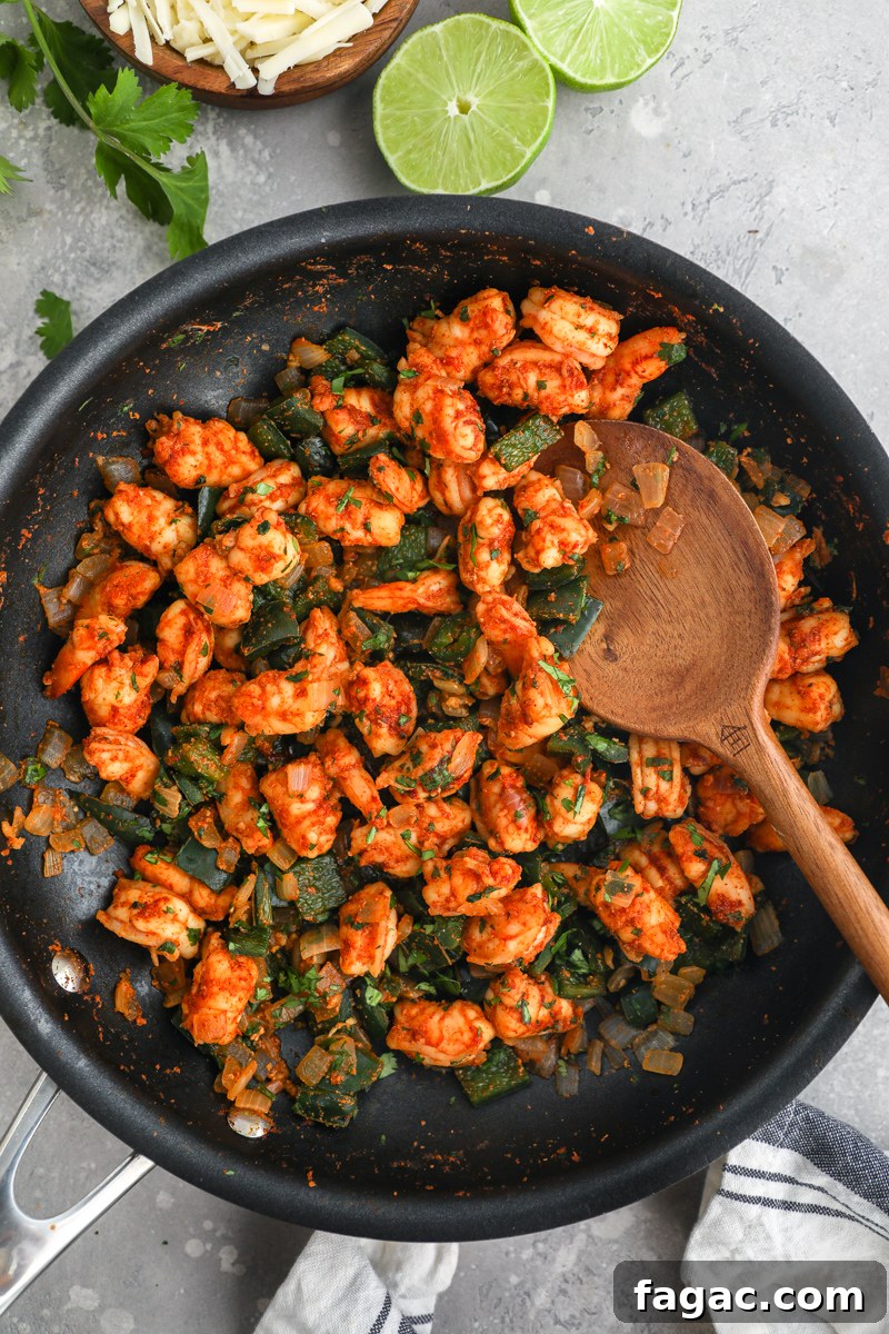 Crispy Shrimp and Poblano Tacos with Avocado Cilantro Sauce 5 A large black skillet filled with sauteed seasoned shrimp, chopped poblano peppers and onions surrounded by fresh lime wedges, cilantro and a small bowl of shredded Monterrey jack cheese