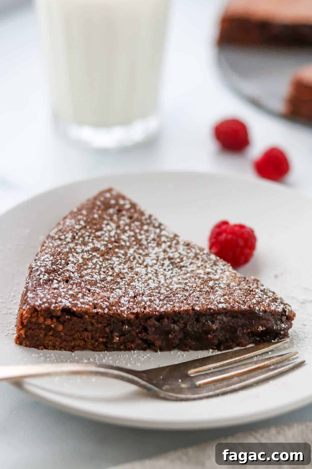 Authentic Swedish Kladdkaka: Gooey Sticky Chocolate Cake Recipe 2 Slice of Swedish Sticky Chocolate Cake (Kladdkaka) dusted with powdered sugar on a plate next to a fork, raspberries and a glass of milk.