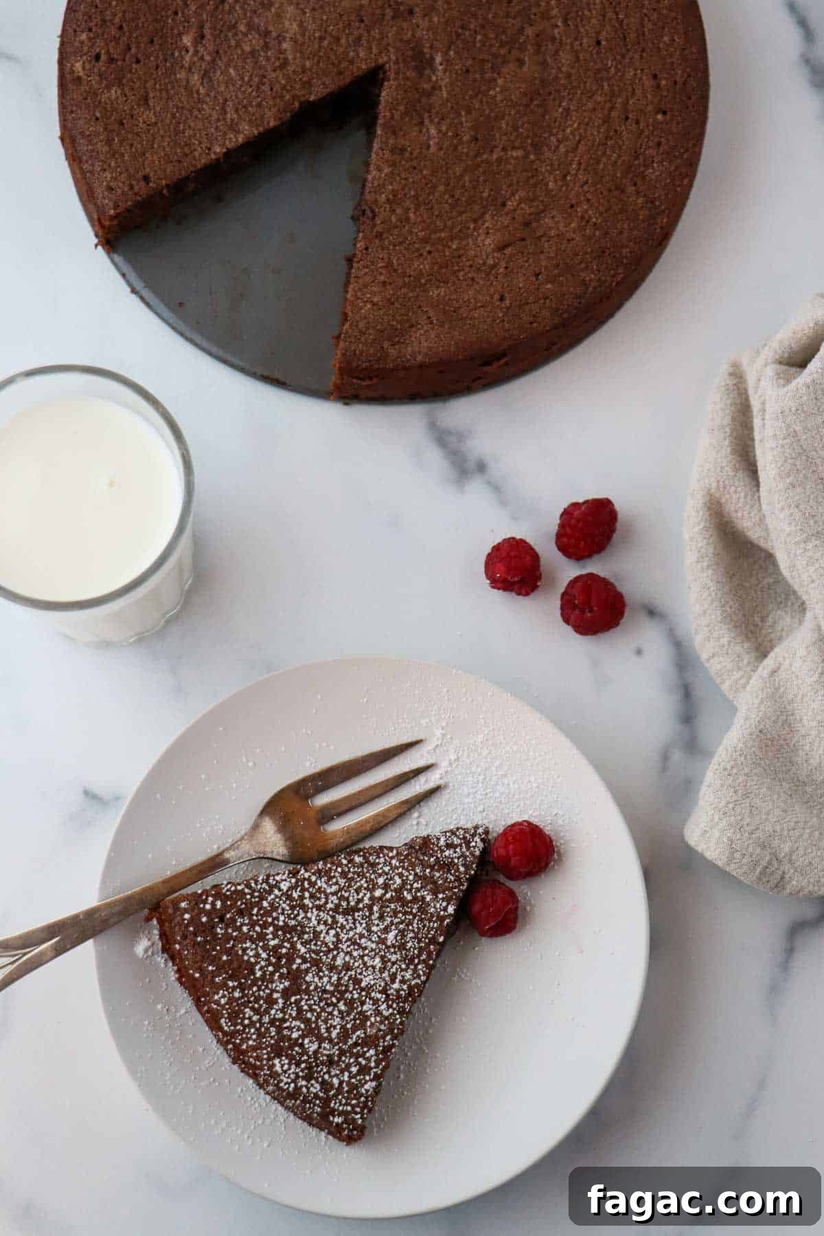 Authentic Swedish Kladdkaka: Gooey Sticky Chocolate Cake Recipe 9 Overhead shot of a slice of kladdkaka on a plate next to raspberries, milk and the whole cake.