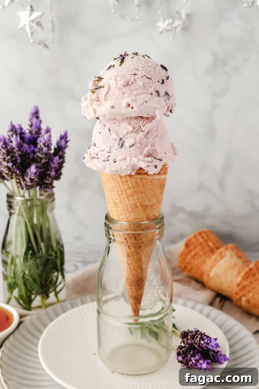 Homemade Lavender Ice Cream Recipe with Creamy Floral Flavor 9 2 scoops of lavender ice cream in a cone with fresh lavender flowers in the background.