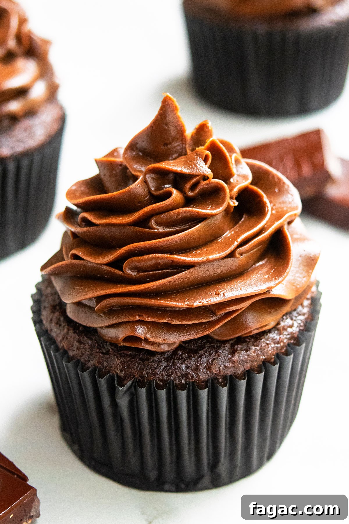 Soft, Moist Chocolate Cupcakes That Melt in Your Mouth 4 Frosted Soft And Moist Cocoa Cupcakes in Black Liner on White Marble Background.
