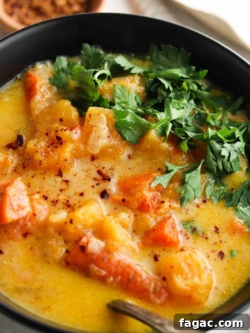 Carrot and butternut squash soup in a black bowl with fresh parsley on top.