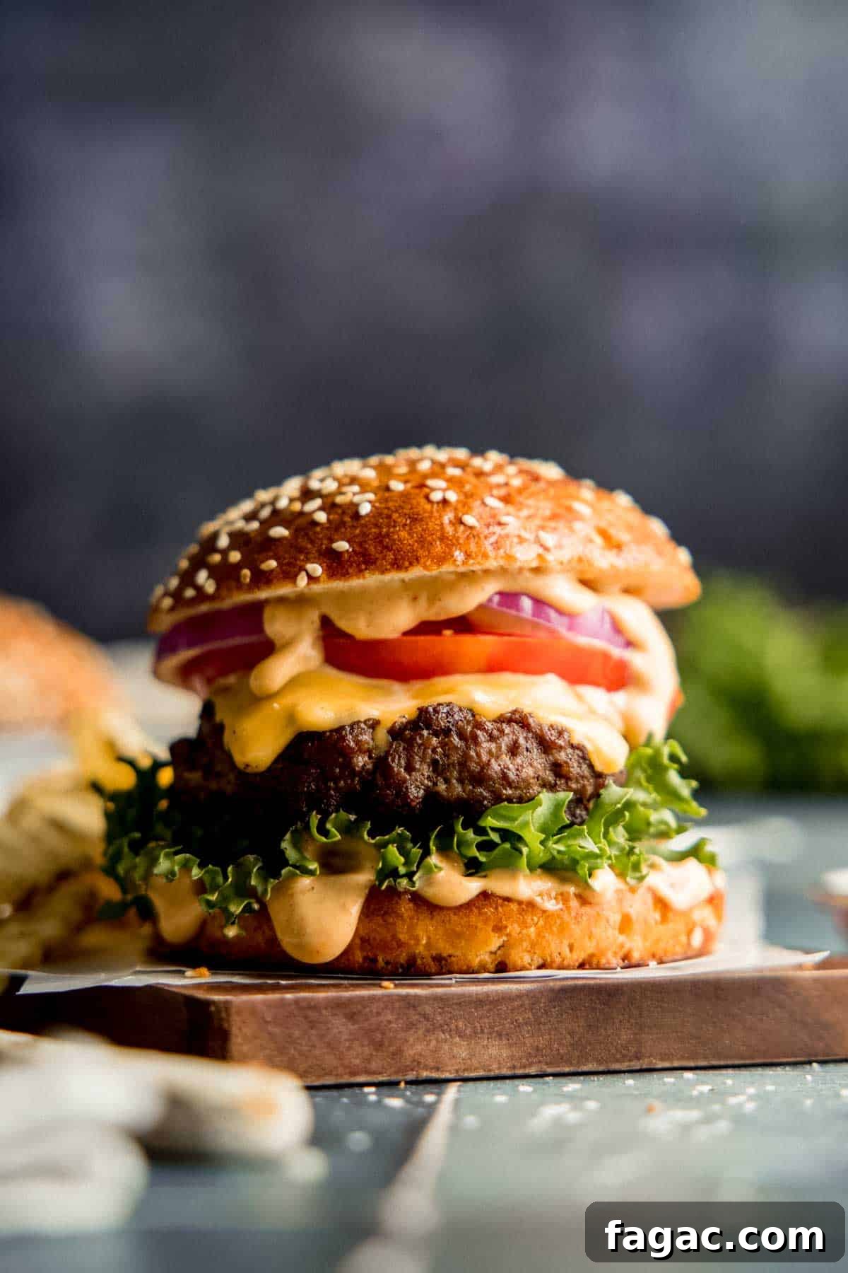 A gluten-free burger with lettuce, tomato, onion, and sauce on a gluten-free bun with sesame seeds.